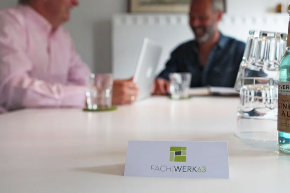 Zwei Personen an einem Besprechungstisch. Im Vordergrund eine Karte mit dem Fachwerk63-Logo.