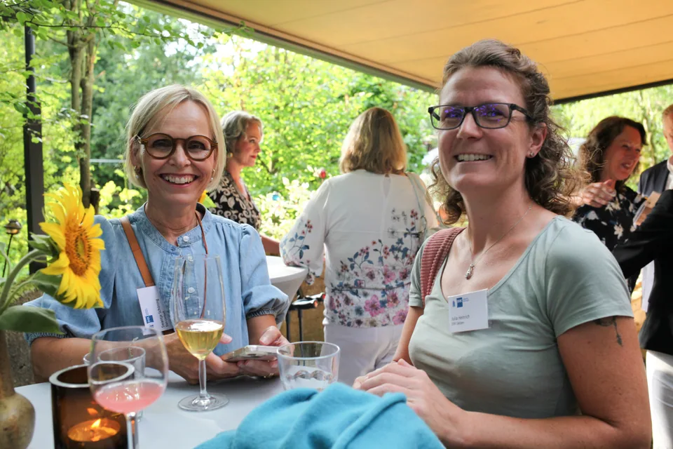 Zwei lächelnde Veranstaltungsgäste an einem Tisch auf der überdachten Terrasse.