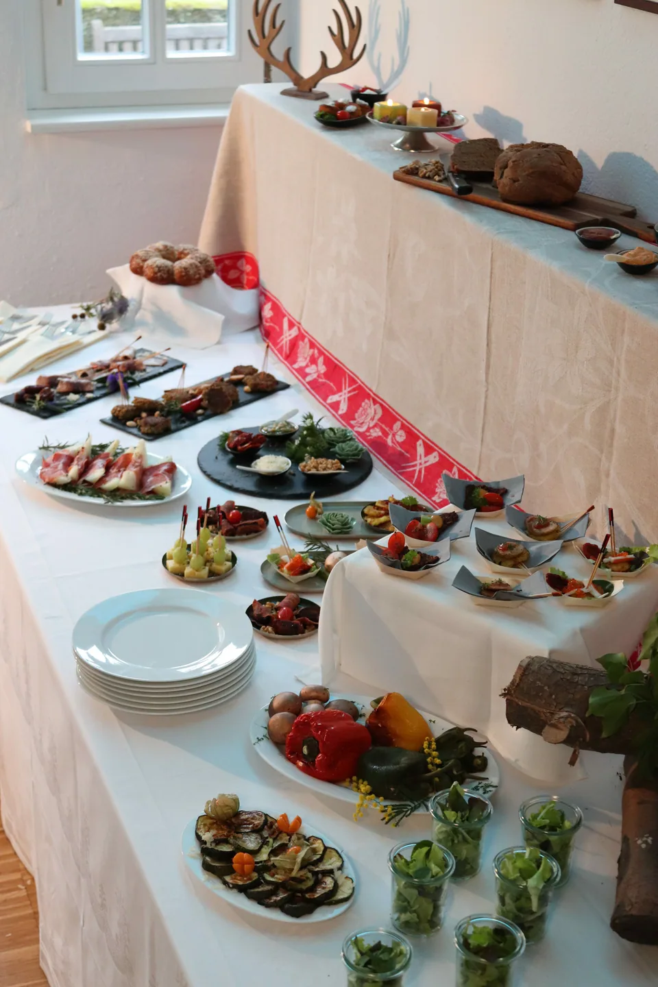 Buffet mit kleinen Portionen auf mehreren Ebenen, Brot und bereitgelegtem Besteck.